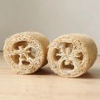 Two natural loofah sponges displayed side by side showing fibrous cross-section texture on a wooden surface.