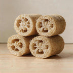 Four natural loofah sponges stacked in a pyramid showing fibrous cross-sections on a wooden surface.