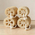 Four natural loofah sponges stacked in two rows on a light wooden background.