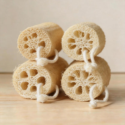 Four natural loofah sponges stacked in two rows on a light wooden background.