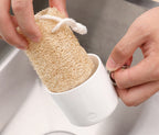 Hand placing a natural loofah sponge into a white kitchen holder for storage.