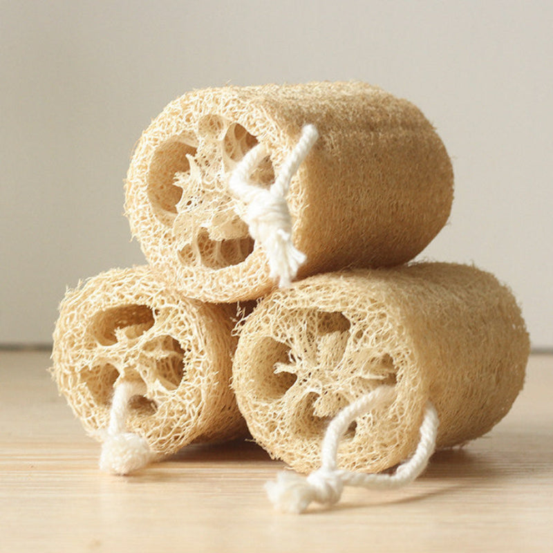Three natural loofah sponges stacked on a light wooden background. Main image