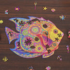 Colorful fish-shaped wooden puzzle with ocean-themed whimsy pieces including seahorse, starfish, anchor, and coral.