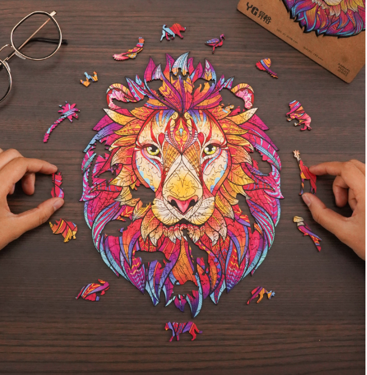 Vibrant lion head wooden puzzle with mandala patterns and unique animal-shaped pieces being assembled on a dark wood table. Main image