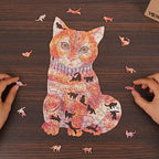 Hands assembling a colorful orange tabby cat-shaped wooden puzzle with cat-shaped whimsy pieces scattered on a dark wood table.